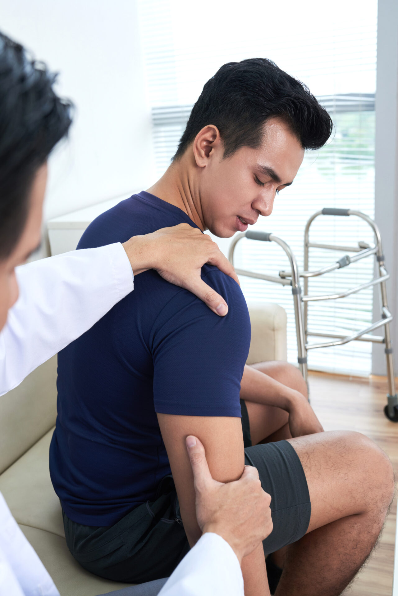 Vertical shot of unrecognizable professional physiotherapist examining sporty young man palpating his shoulder