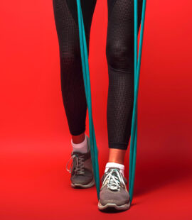 Close up of female legs in sportswear with expander exercising over red background
