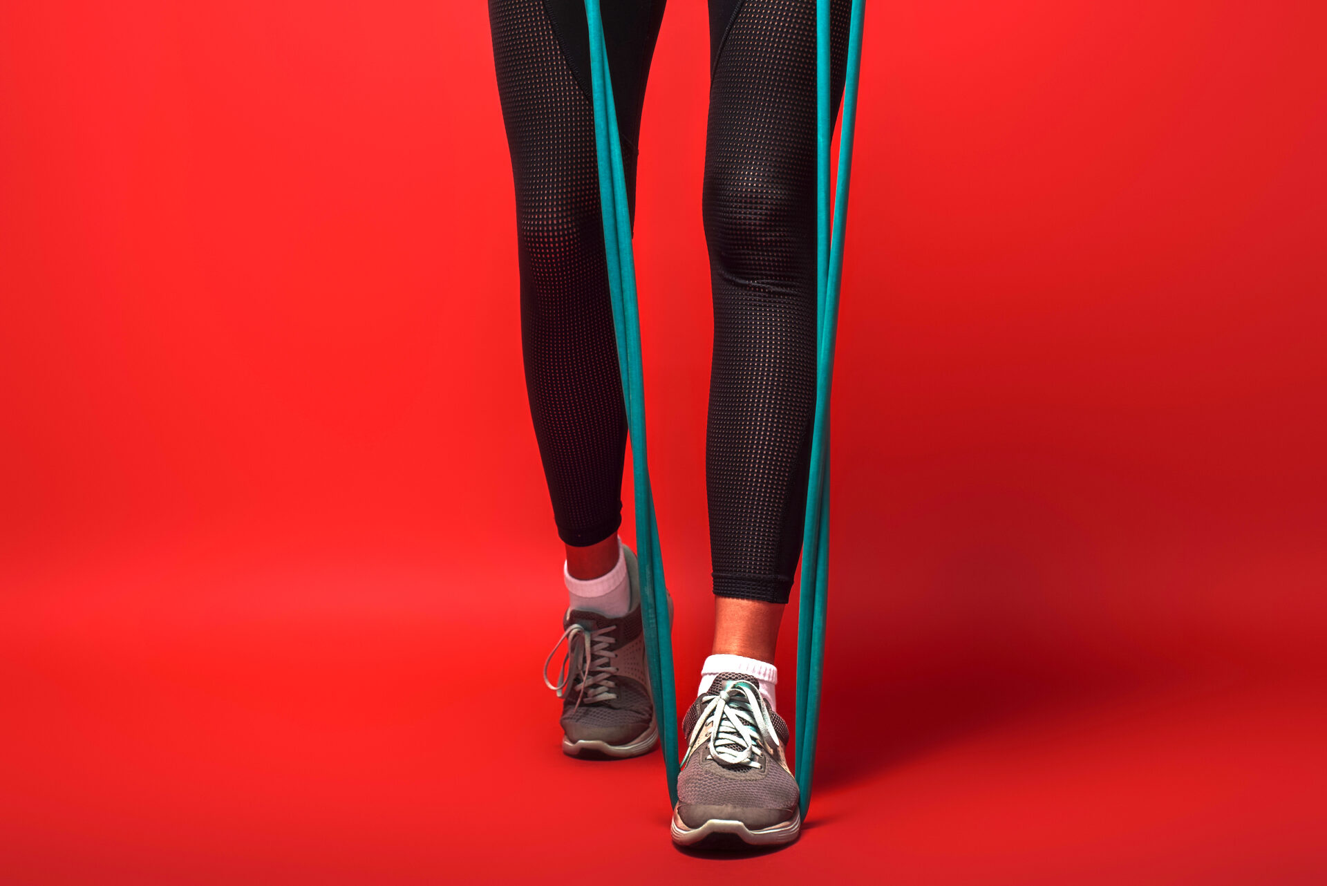 Close up of female legs in sportswear with expander exercising over red background