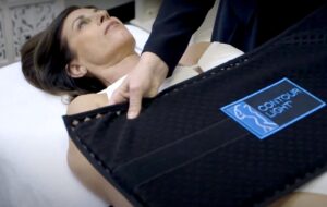 a practitioner gently applies the Contour Light red light therapy pads onto the abdomen of a female patient clothed in bathing suit